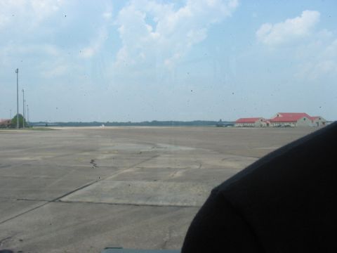 1988 Ford Bronco - View from inside a vehicle looking out at an airport tarmac with buildings and a distant aircraft under a cloudy sky.