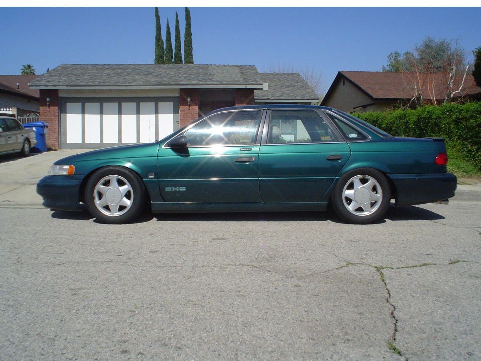 Lowered green Ford Taurus SHO sedan profile parked outside a brick house