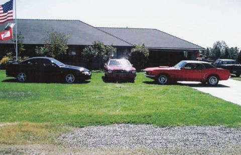 1978 Ford Mustang II - Three Ford Mustangs parked in front of a house, including a red 1969 fastback.