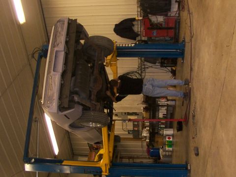1978 Ford Mustang II - A mechanic works on the underside of a car elevated on a lift in a workshop.
