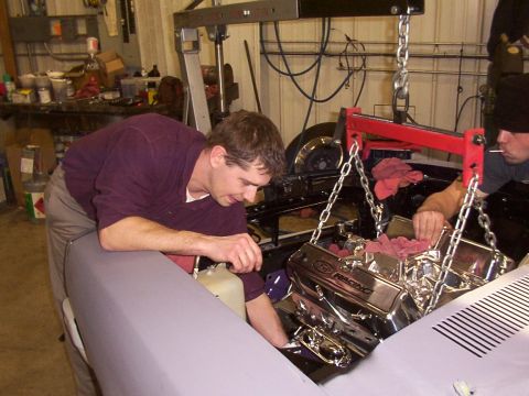 1978 Ford Mustang II - Mechanics work on installing a chrome engine into a vehicle, with a Supermotors watermark visible at the bottom right.