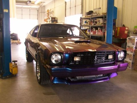 1978 Ford Mustang II - A 1978 Ford Mustang II with a custom paint job is parked in a garage, showing its front grille and headlights.