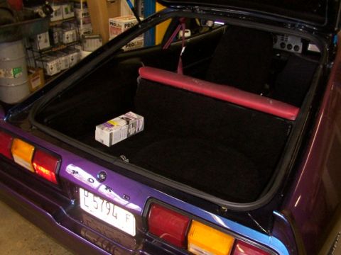 1978 Ford Mustang II - The interior of a purple 1978 Ford Mustang II hatchback, showing the trunk area with a small box and the rear seats.