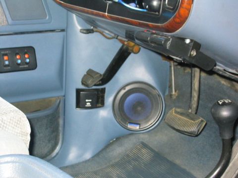 1989 Ford Bronco - Driver's footwell of a light blue truck interior showing a kick-panel-mounted speaker with a blue cone, brake and accelerator pedals, a par…