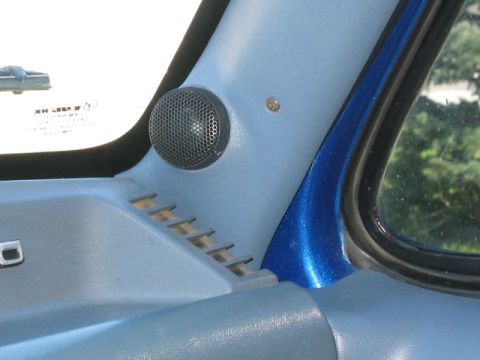 1989 Ford Bronco - Close-up of a mesh-grilled tweeter flush-mounted in the light blue A-pillar trim beside the windshield, with dash defrost vents below and a…