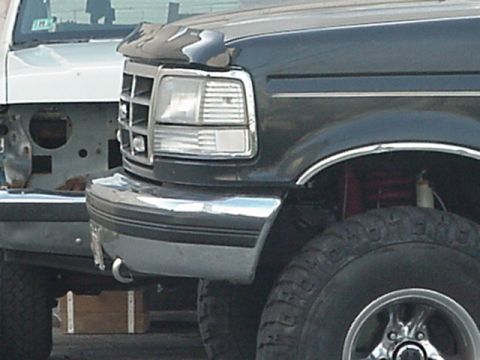 1993 Ford Bronco - Front corner of a dark truck a chrome grille and bumper, with another vehicle partially visible behind.