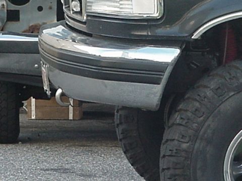 1993 Ford Bronco - Close-up of a 1993 Ford Bronco's front bumper and tire, with another vehicle in the background.