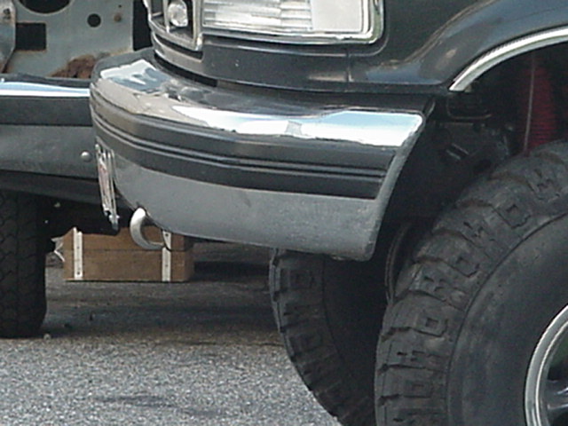 1993 Ford Bronco front bumper with chrome trim and tow hook; another vehicle is partially visible to the left