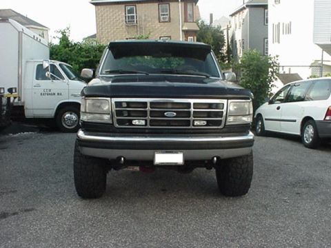 1993 Ford Bronco - Front view of a black Ford Bronco with aftermarket modifications, parked outdoors with other vehicles.