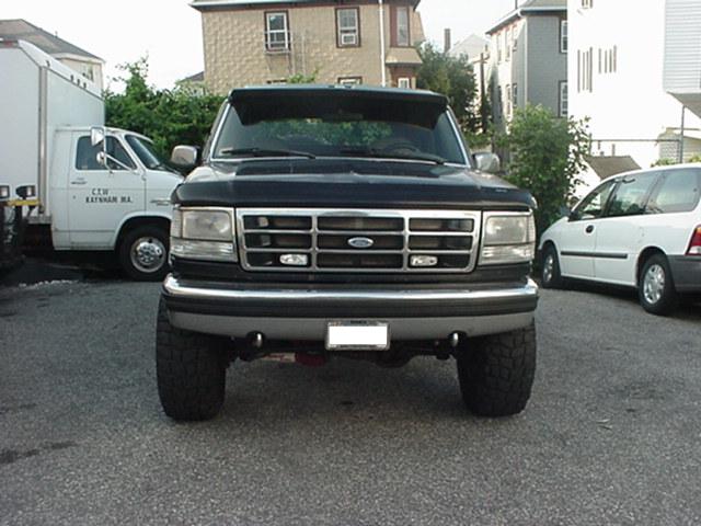 Black Ford Bronco front view, lifted with large tires. White van and white minivan in background
