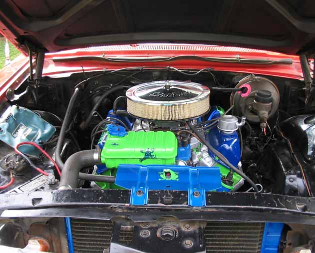 Engine bay of red Ford Galaxie with chrome Edelbrock air cleaner, blue engine and green painted accents