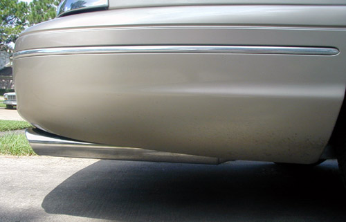 Rear lower corner of tan sedan with chrome exhaust tip under bumper on driveway