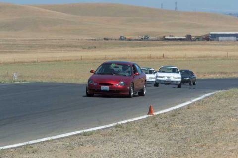 1997 Ford Taurus - A red sedan leads other vehicles on a sunny day at a racetrack.