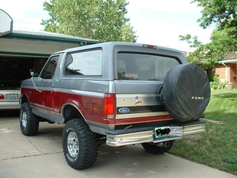 1994 Ford Bronco - This Ford Bronco has a two-tone paint job and a spare tire mounted on the rear door. A basketball hoop is visible in the background.