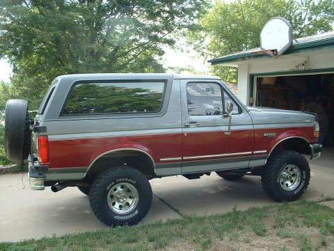 1994 Ford Bronco - A side view of a lifted Ford Bronco with a two-tone paint scheme and off-road tires.