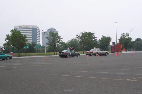 2001 Mercury Grand Marquis - Sedans are parked in a lot with cones, with office buildings visible in the distance.