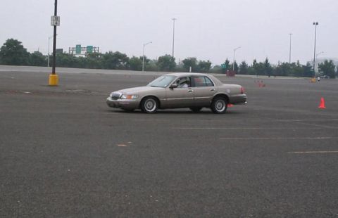 2001 Mercury Grand Marquis - A tan Mercury Grand Marquis is shown on a paved lot, possibly during a driving event with orange cones marking a course.