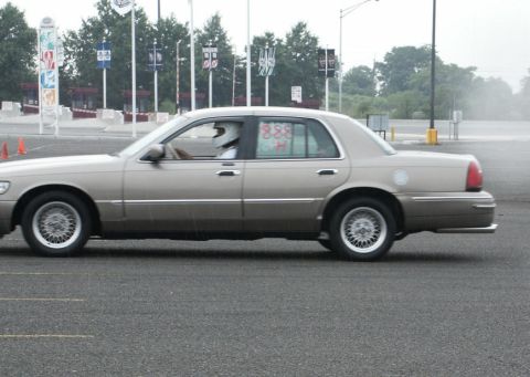 2001 Mercury Grand Marquis - A 2001 Mercury Grand Marquis sedan is seen from the side, with a driver wearing a helmet.