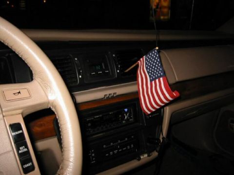 1992 Ford Crown Victoria - The interior of a car shows a dashboard with an American flag hanging from the air vent and a digital clock displaying 0:32.