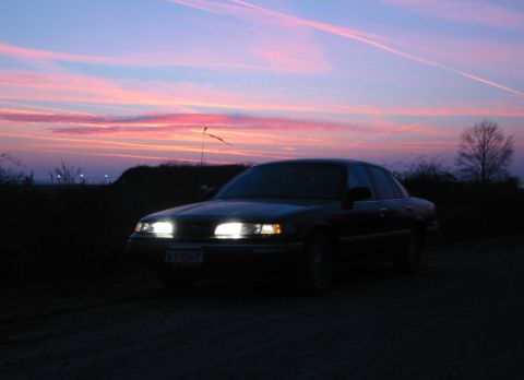 1992 Ford Crown Victoria - 1992 Ford Crown Victoria sedan parked with headlights on during a colorful sunset.