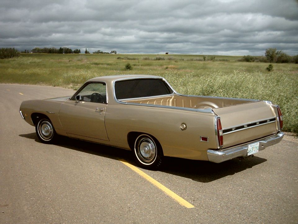 Gold coupe utility pickup seen from rear three-quarter on a rural road under cloudy sky