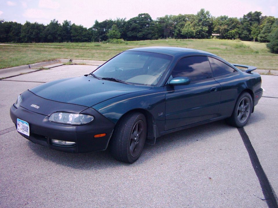 Dark green Mazda MX-6 coupe, 3q-front view with bra and alloy wheels in a lot