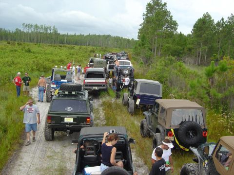1993 Ford Bronco - A convoy of off-road vehicles navigates a dirt track through a wooded and grassy area.