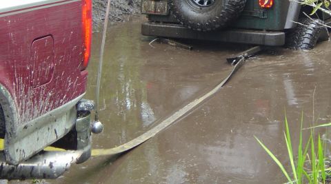 1993 Ford Bronco - Two vehicles are stuck in the mud, with one being pulled out by a tow strap.