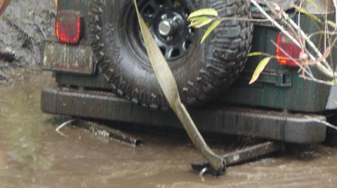 1993 Ford Bronco - A green SUV is stuck in the mud, showing its rear bumper and spare tire with a tow strap.