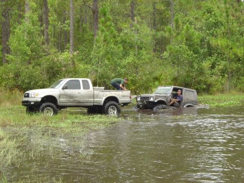 1993 Ford Bronco - Two off-road vehicles are stuck in water, with one truck attempting to tow the other.