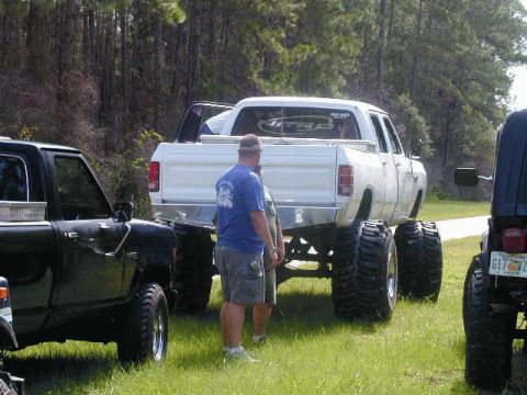 1993 Ford Bronco - A lifted white Dodge pickup truck is parked on grass with other vehicles nearby.
