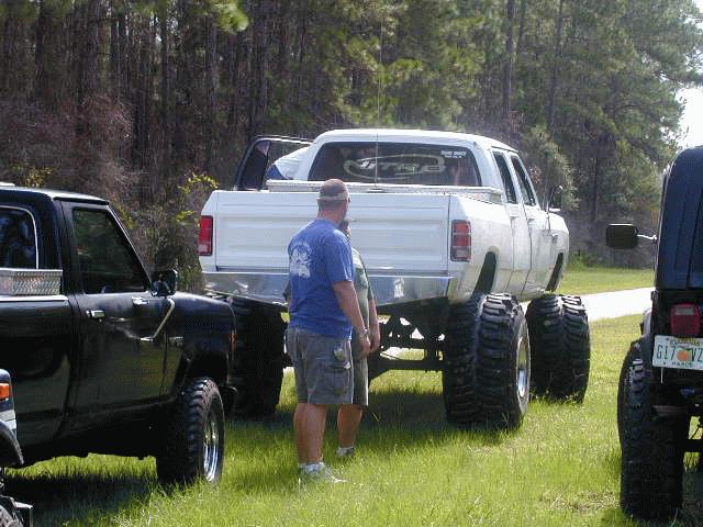 White Dodge pickup with huge tires, parked next to a black truck and a Jeep