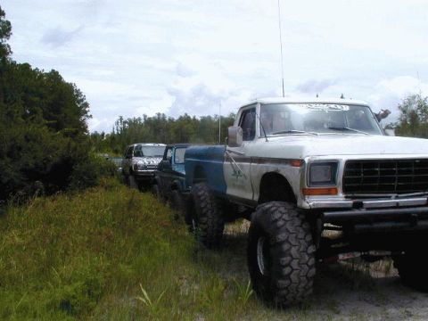 1993 Ford Bronco - A line of off-road vehicles, including a modified Ford pickup, are parked on a dirt path.