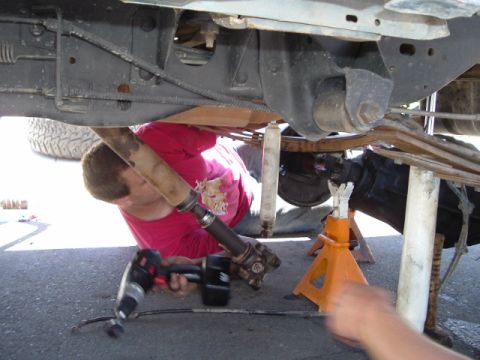 1989 Ford Bronco - A mechanic works on the rear axle and driveshaft of a vehicle lifted on jack stands.