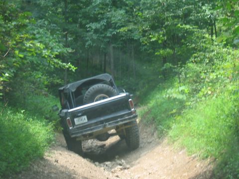 1988 Ford Bronco - Off-road vehicle navigating a rocky dirt path surrounded by dense green foliage.