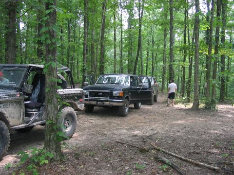 1988 Ford Bronco - Multiple off-road vehicles are parked in a wooded area, with one Bronco in the foreground.