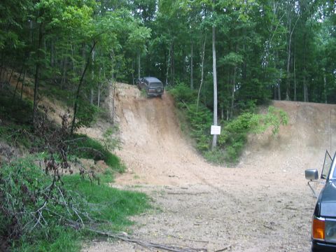 1988 Ford Bronco - Off-road vehicles navigate a steep dirt incline surrounded by dense forest.