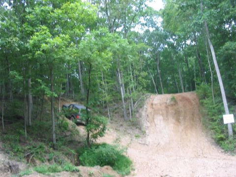 1988 Ford Bronco - A dark SUV navigates a challenging dirt incline surrounded by dense forest foliage.