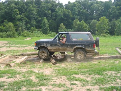 1988 Ford Bronco - A muddy Ford Bronco drives over logs on an off-road course.