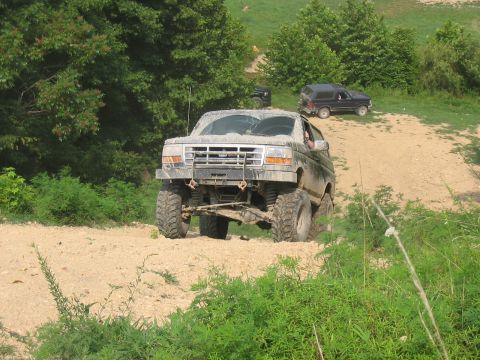 1988 Ford Bronco - This modified Ford Bronco is navigating a dirt path, with other vehicles visible in the distance.