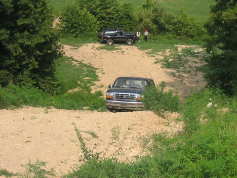 1988 Ford Bronco - A dark blue Ford F-150 navigates a dirt path, with another SUV visible further up the trail.