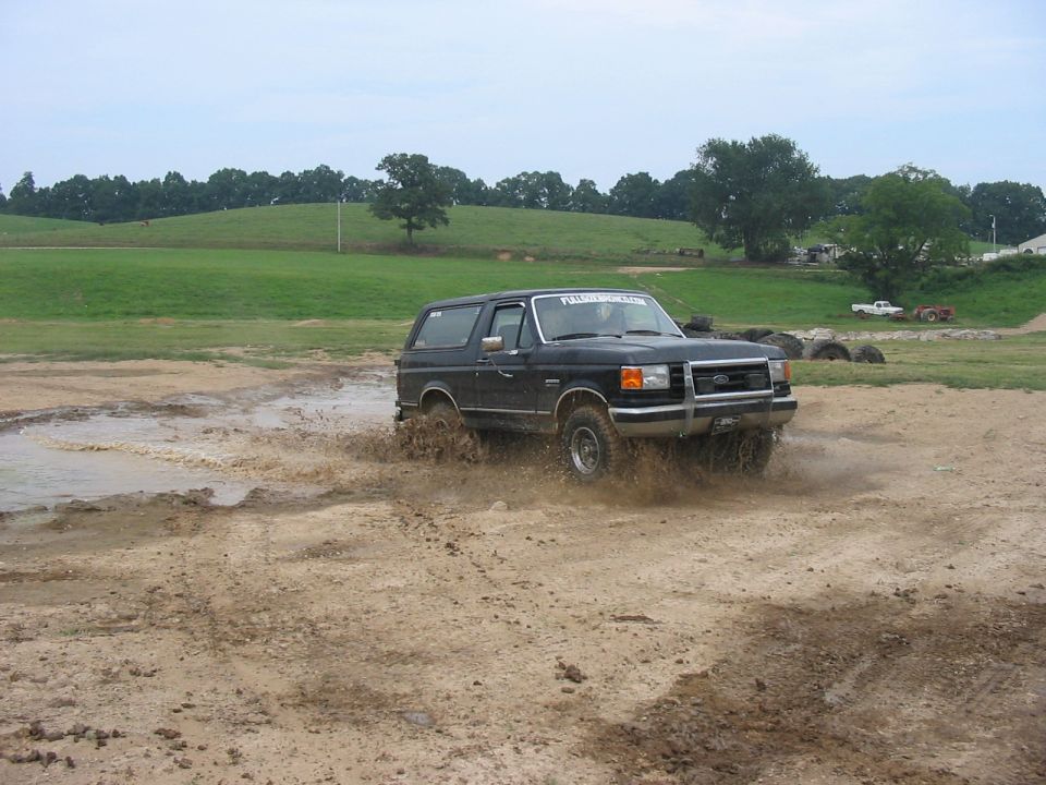 Black 1988 Ford Bronco driving through mud