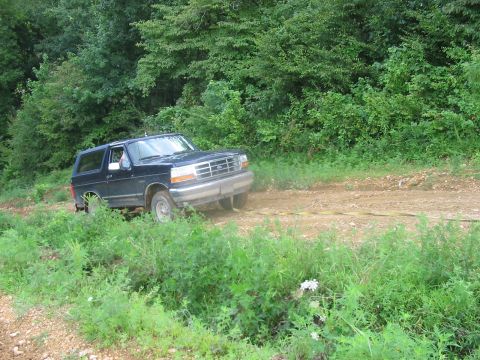 1988 Ford Bronco - Dark blue SUV on a dirt road, possibly stuck or being towed.