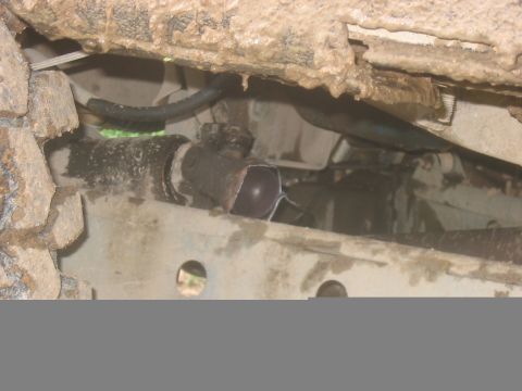 1988 Ford Bronco - Close-up view of the dirty undercarriage of a vehicle, revealing mechanical parts and a hose.