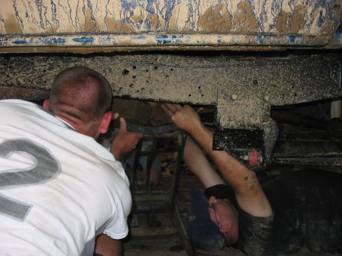 1988 Ford Bronco - Two individuals are inspecting the undercarriage of a heavily soiled vehicle, possibly for repairs or modifications.