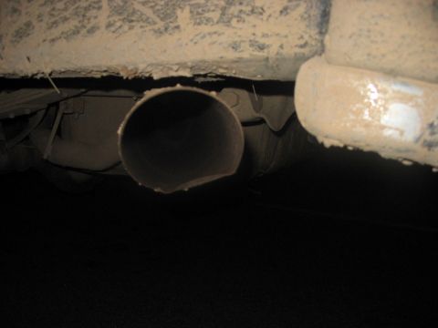 1988 Ford Bronco - Close-up view of a vehicle's exhaust pipe and the underside of its body, covered in dirt.