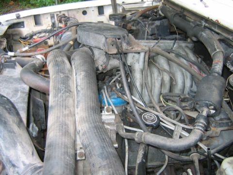 1992 Ford Bronco - Engine bay view of a Ford Bronco showing a dusty V8 engine with intake manifold, radiator hoses, wiring, and a black oil filler cap labeled…