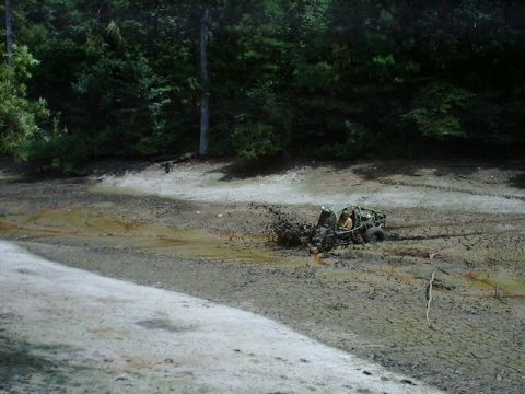 1993 Ford Bronco - An off-road vehicle is stuck in the mud near a wooded area.