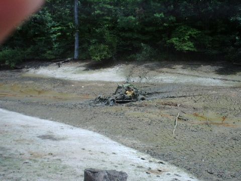 1993 Ford Bronco - An off-road buggy is stuck in thick mud near a wooded area.