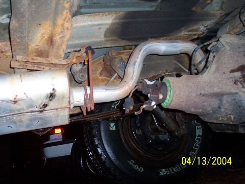 1994 Ford Bronco - The underside of a vehicle reveals its exhaust system and rear axle components, with visible rust and wear.